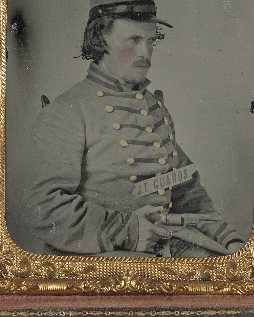 A dark, tarnished tintype of a Confederate corporal holding a revolver.